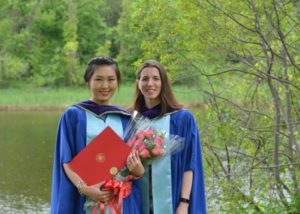 Leah and Sonia in graduation gowns standing by the river on campus