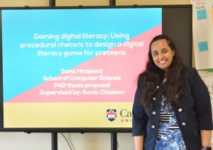 Sana standing next to her title slide for her PhD proposal