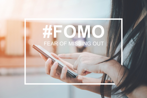 Close up of a girl using a smartphone with the text #FOMO overlaid on the image