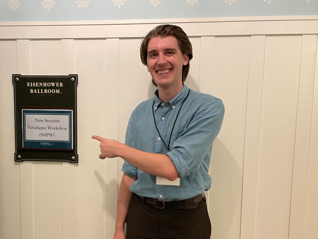 Max at the conference hotel, pointing to a sign saying NSPW