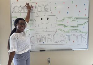 Charlotte smiling in front of the lab whiteboard which says Congrats Charlotte