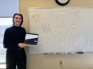 Max standing next to whiteboard in the lab and holding his laptop, celebrating a successful PhD proposal defence