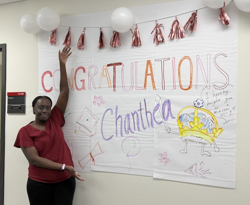 Chanthea standing next to a large Congratulations poster on the wall