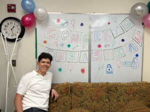 Sebastian next to a decorated whiteboard congratulating him on a successful defence